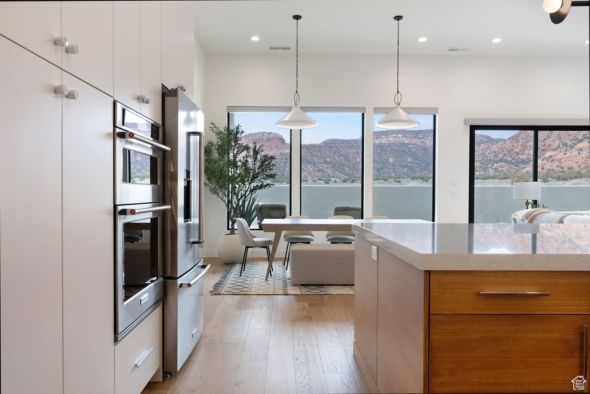 Kitchen with white cabinets, light stone countertops, hanging light fixtures, and light hardwood / wood-style flooring