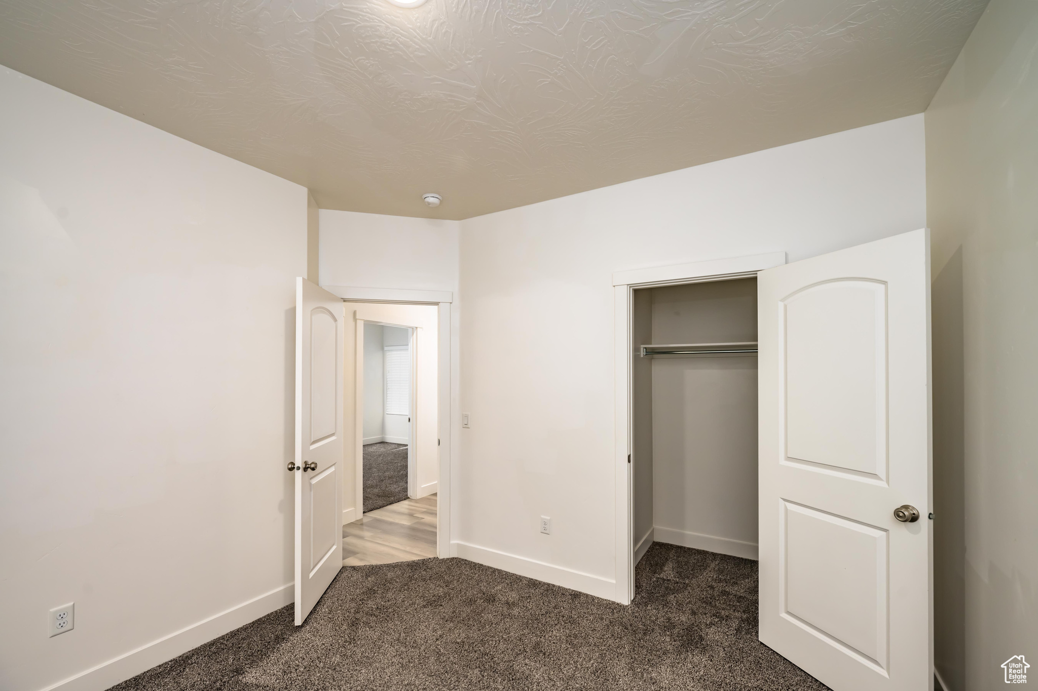 Unfurnished bedroom featuring a closet, dark carpet, and a textured ceiling