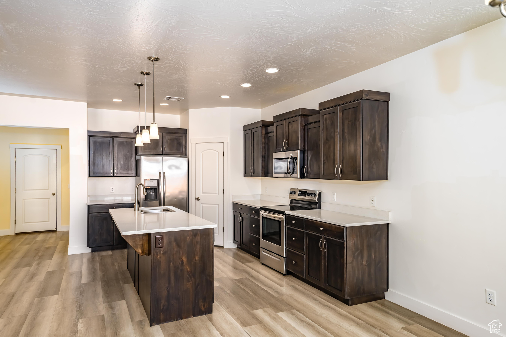 Kitchen with pendant lighting, a center island with sink, sink, dark brown cabinetry, and stainless steel appliances