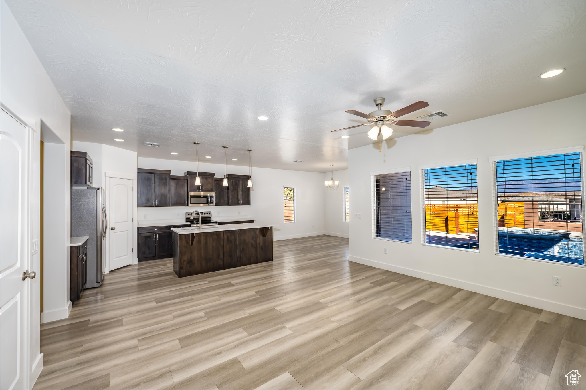 Kitchen with ceiling fan, hanging light fixtures, an island with sink, appliances with stainless steel finishes, and light wood-type flooring