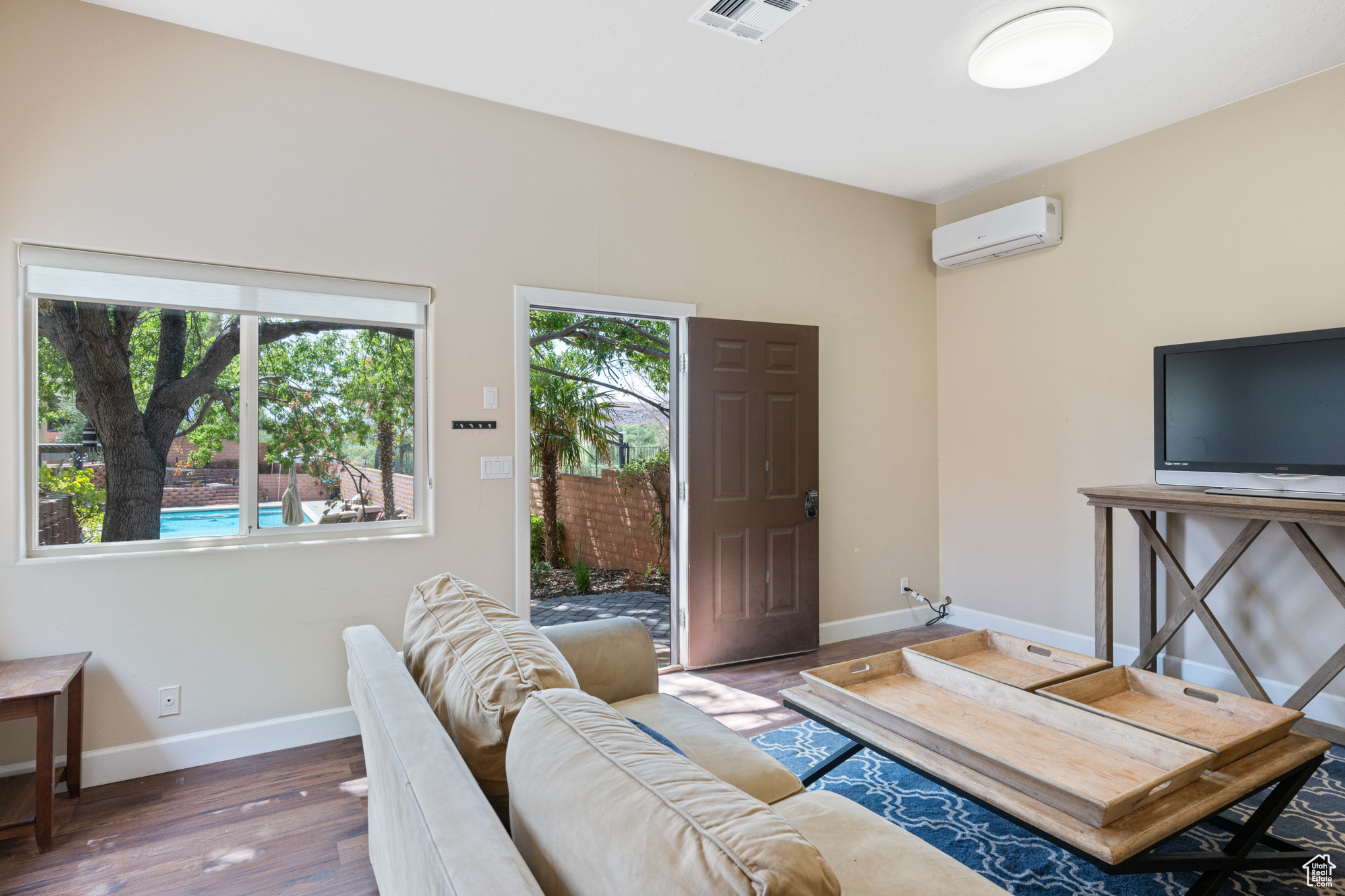 Living room with dark wood-type flooring and a wall mounted air conditioner