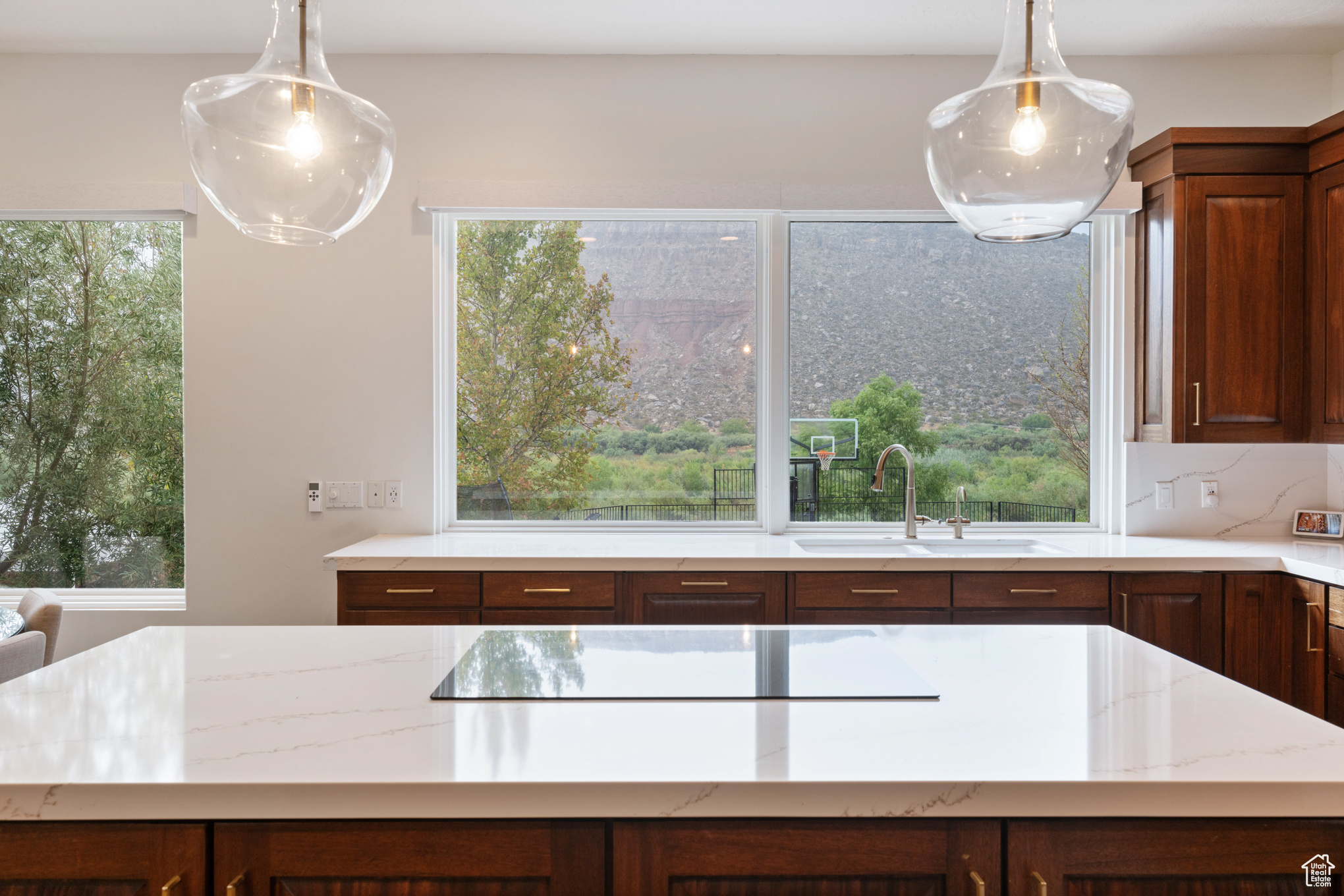 Kitchen featuring black electric cooktop, light stone countertops, sink, and pendant lighting