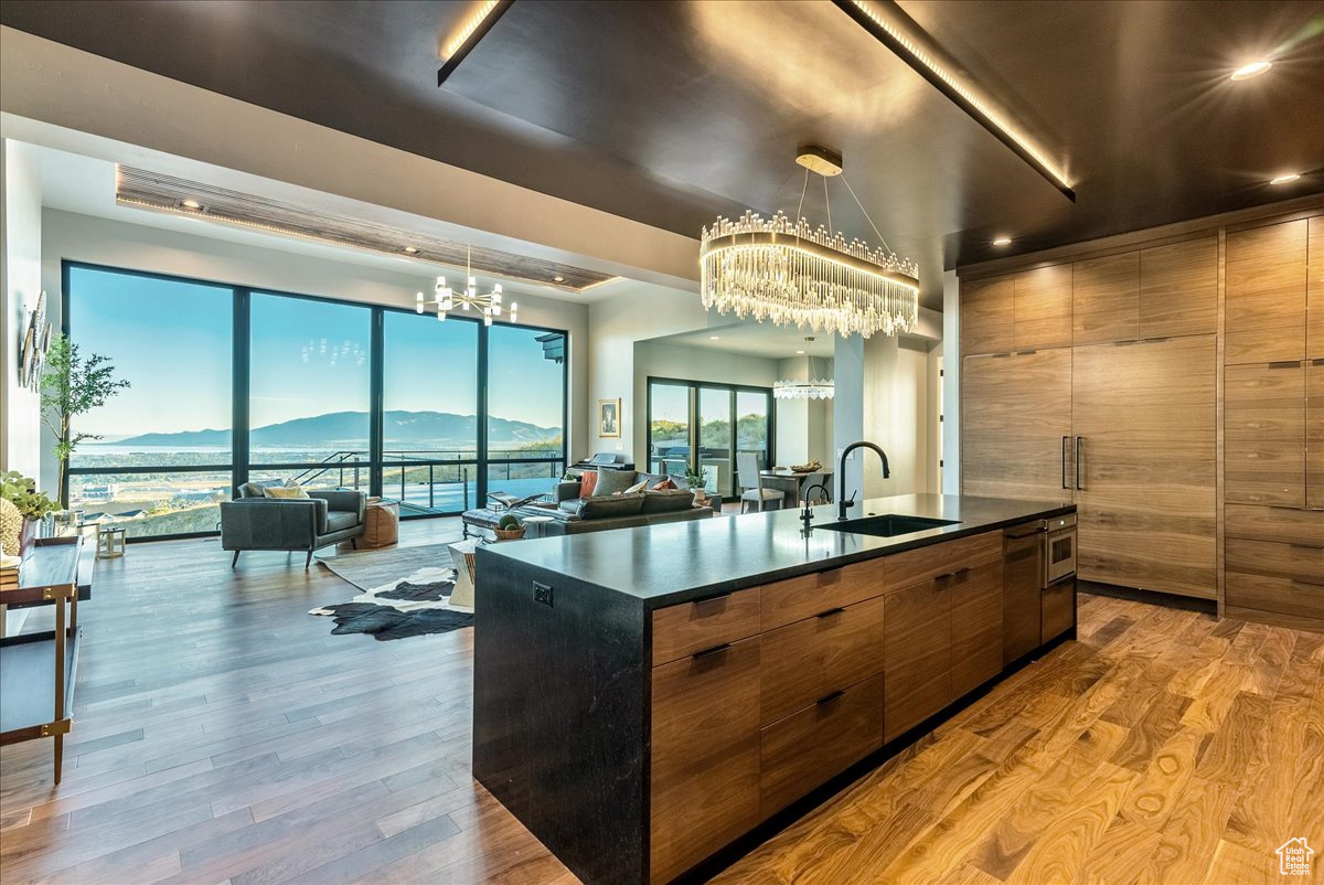 Kitchen with a mountain view, sink, an island with sink, a notable chandelier, and light hardwood / wood-style floors