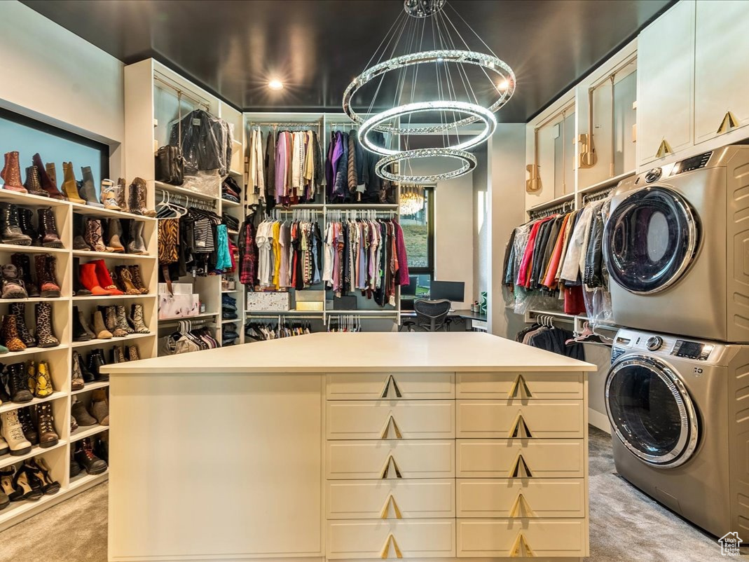 Spacious closet with light colored carpet, an inviting chandelier, and stacked washer and clothes dryer