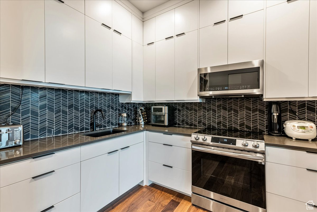 Kitchen with white cabinetry, sink, hardwood / wood-style floors, decorative backsplash, and appliances with stainless steel finishes