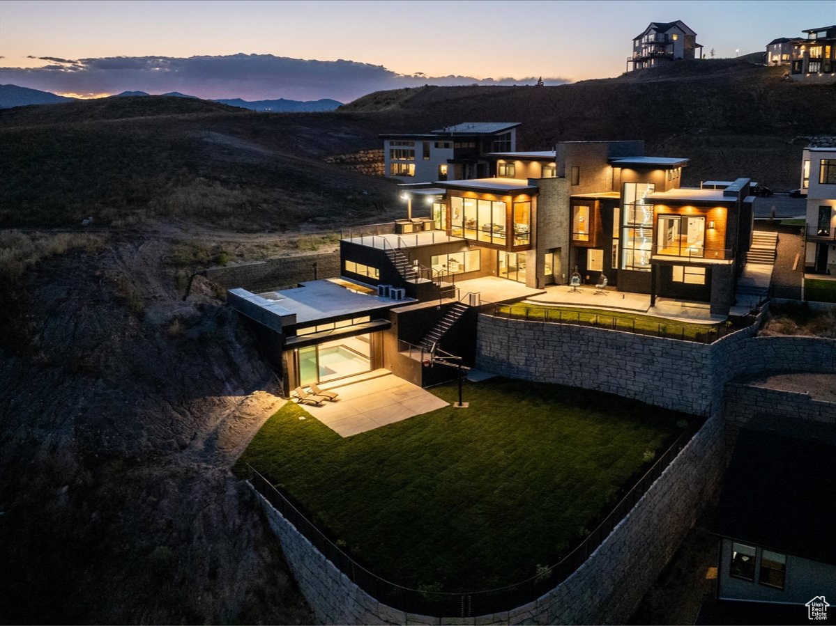 Back house at dusk featuring a lawn, a patio area, and a mountain view