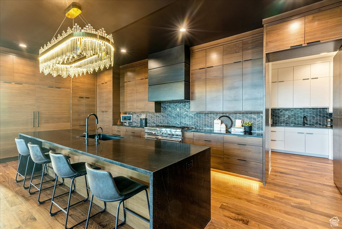 Kitchen with sink, light hardwood / wood-style flooring, wall chimney range hood, and a center island with sink