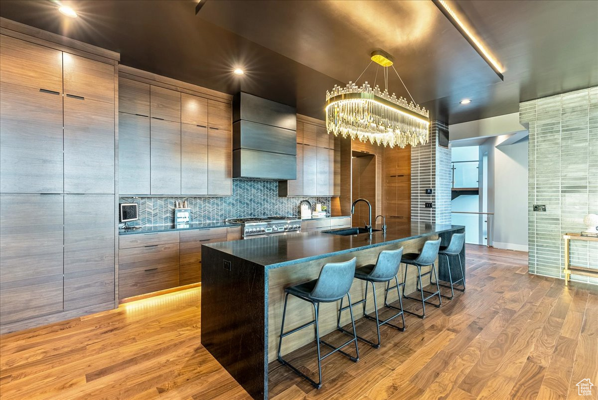 Kitchen with stainless steel range with gas cooktop, sink, light hardwood / wood-style flooring, wall chimney exhaust hood, and an island with sink