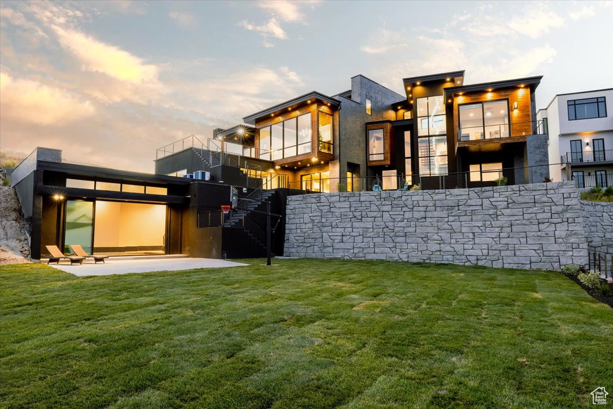 Back house at dusk with a patio area and a lawn