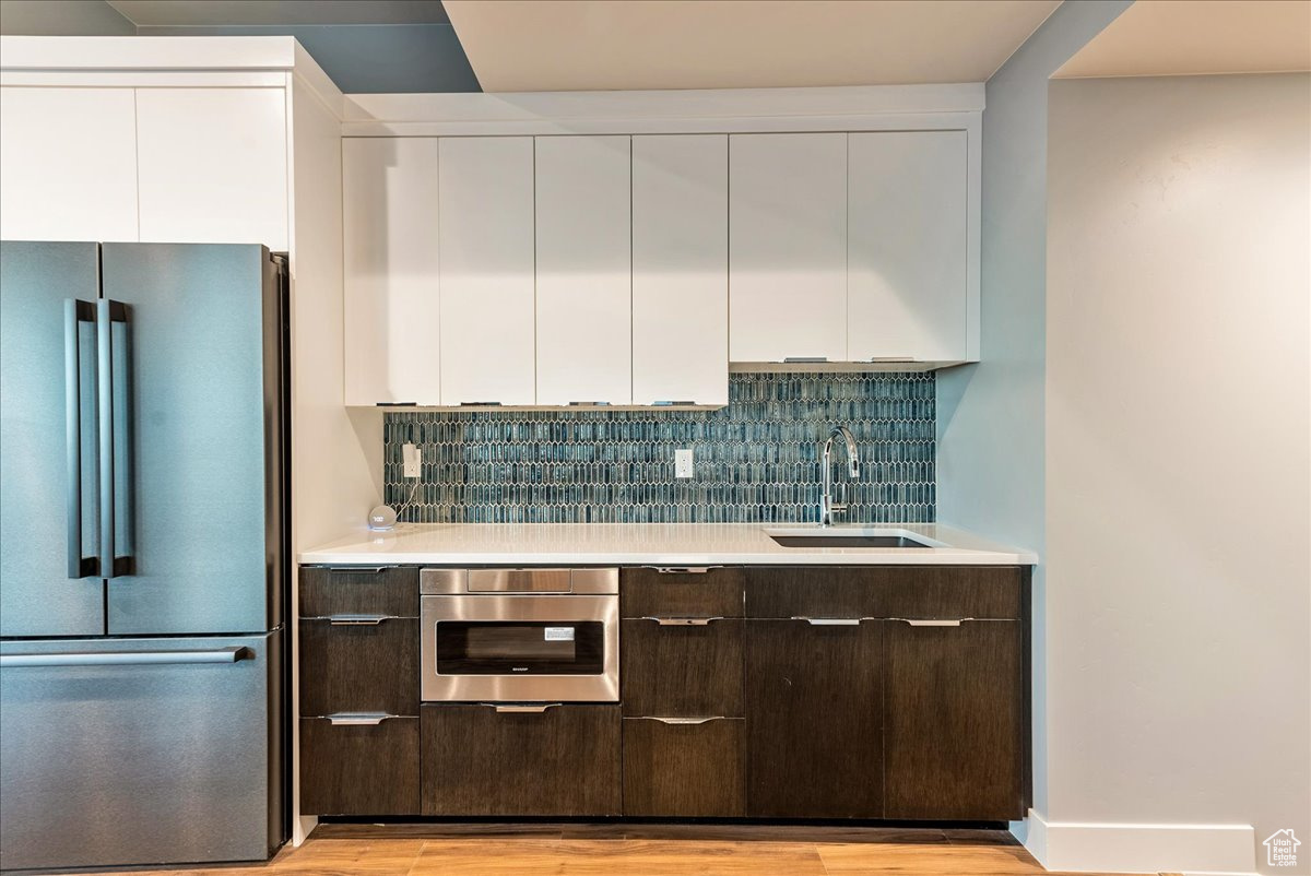 Kitchen with dark brown cabinetry, white cabinetry, sink, wall oven, and stainless steel fridge