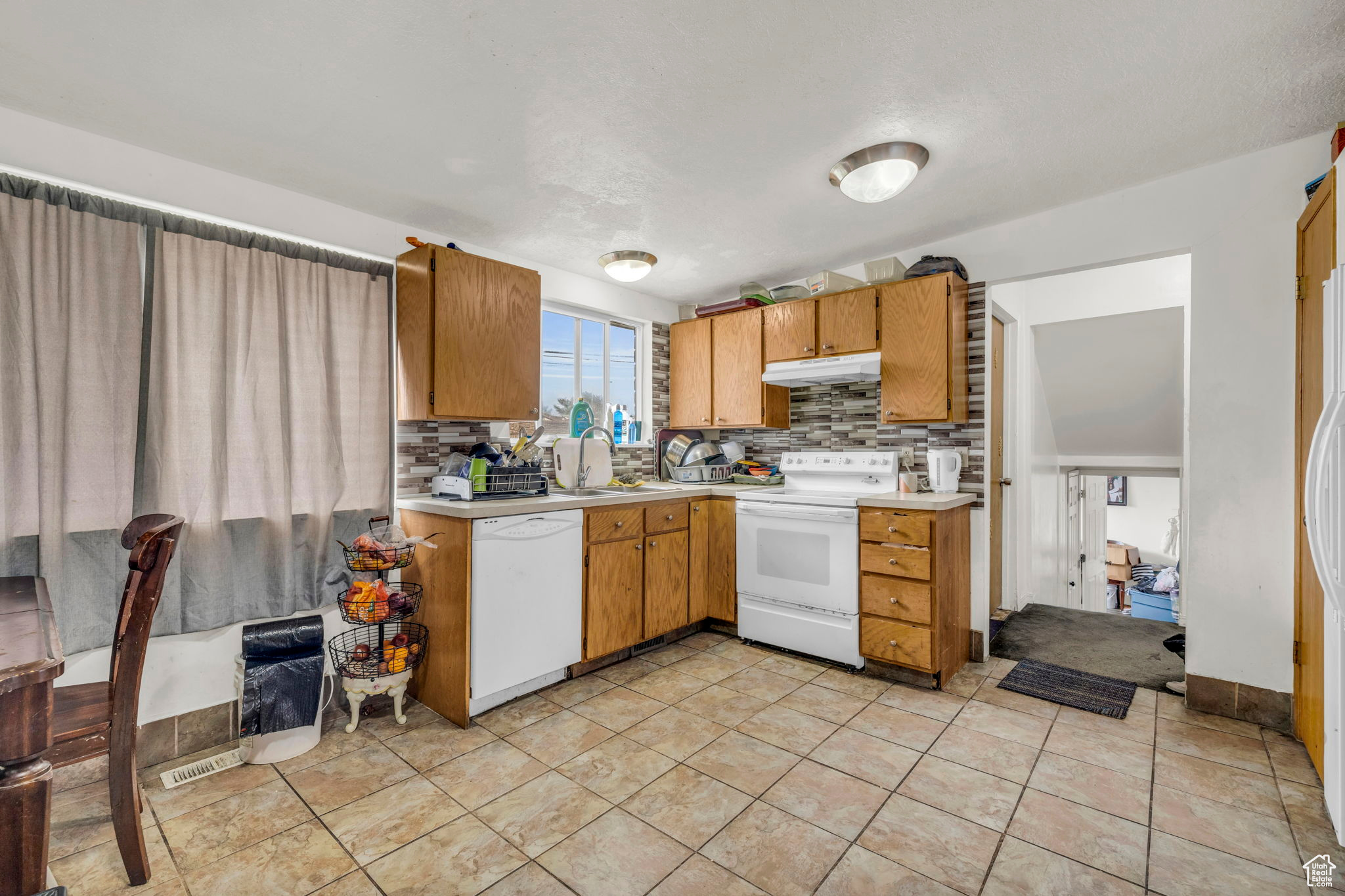 Kitchen featuring decorative backsplash, sink, light tile patterned flooring, and white appliances