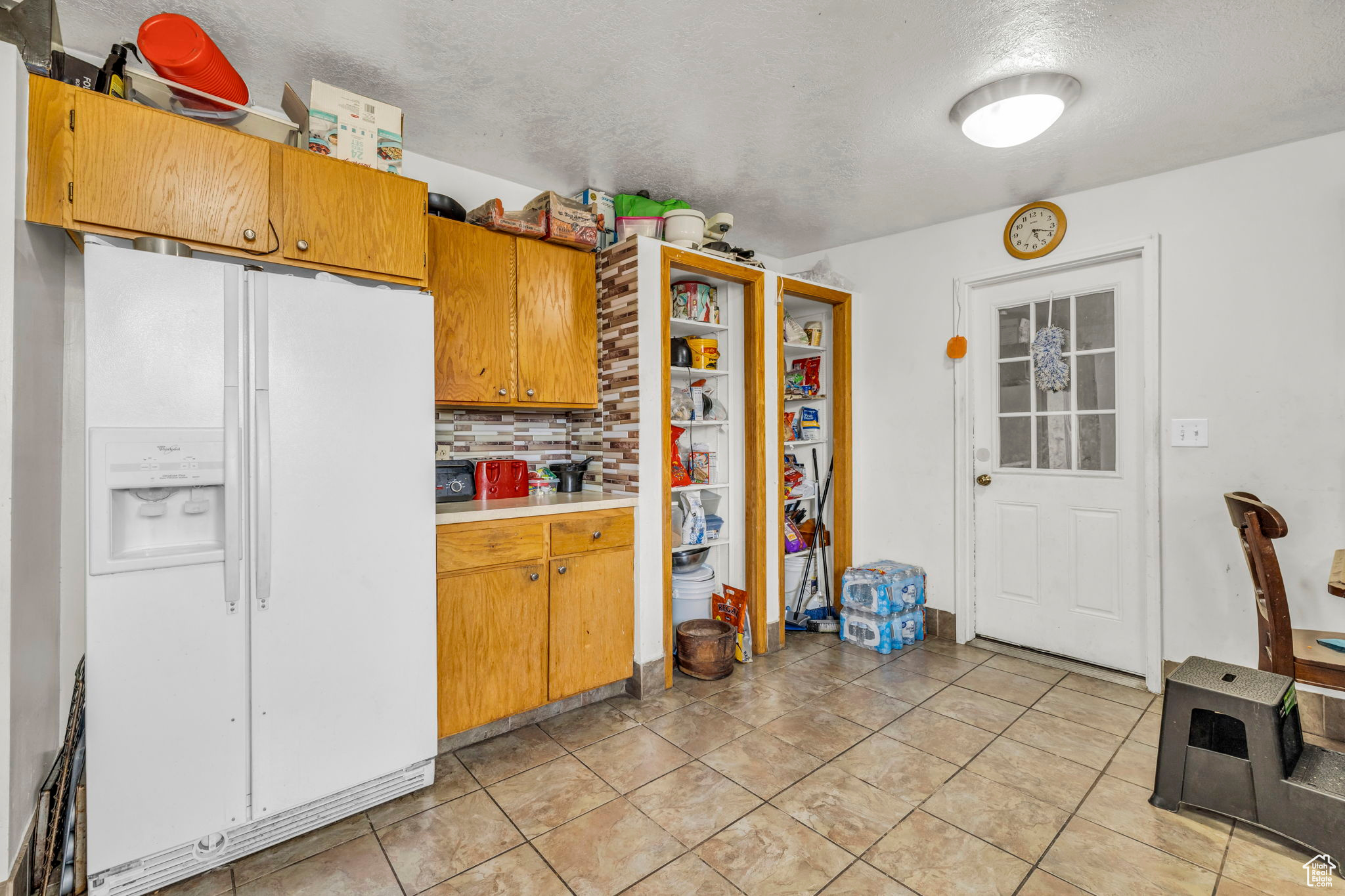 Kitchen featuring tasteful backsplash, a textured ceiling, light tile patterned flooring, and white refrigerator with ice dispenser