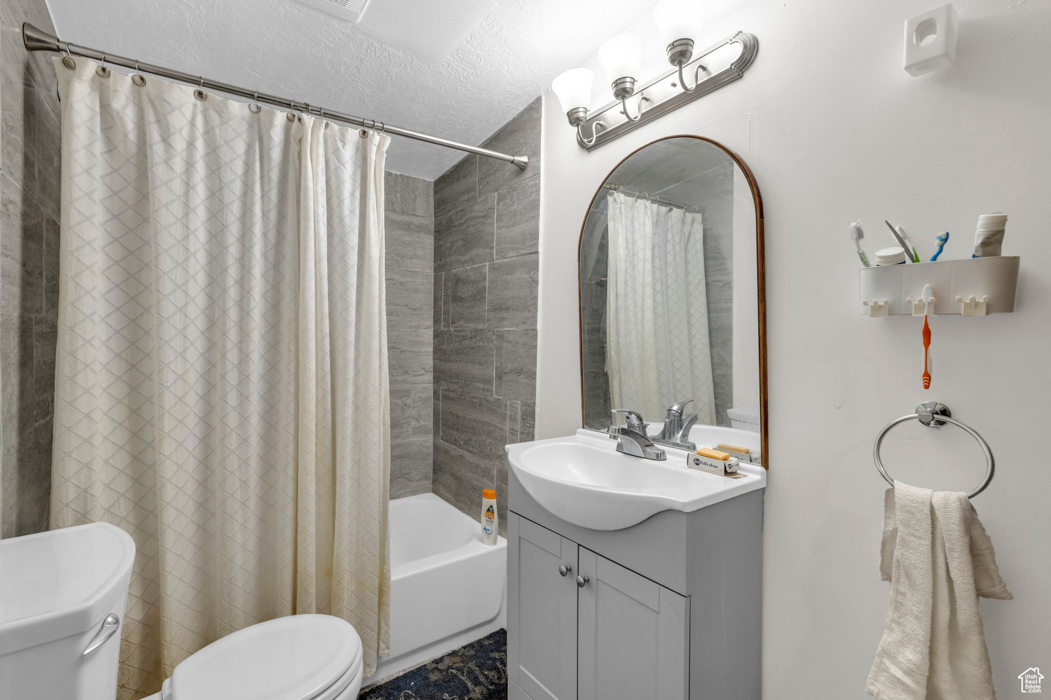 Full bathroom featuring vanity, shower / bathtub combination with curtain, a textured ceiling, and toilet