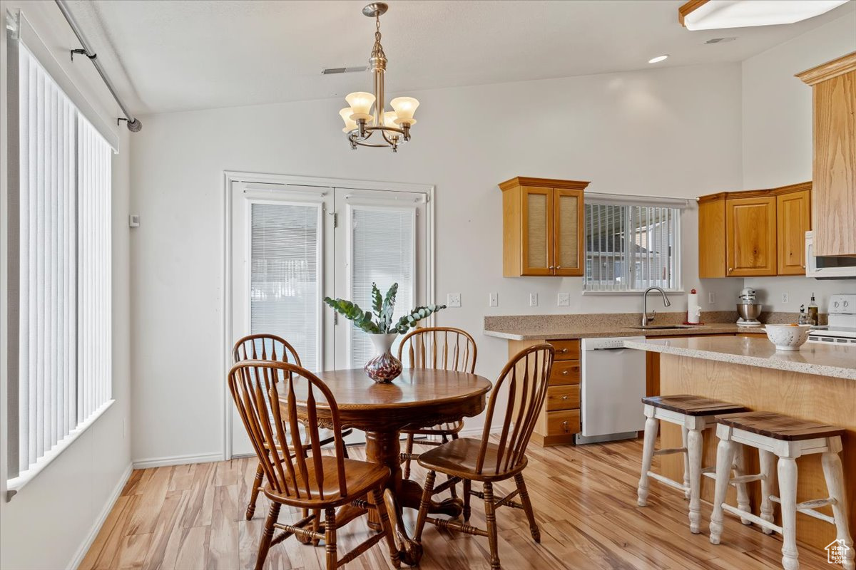 Dining space with light hardwood / wood-style flooring, vaulted ceiling, sink, and an inviting chandelier