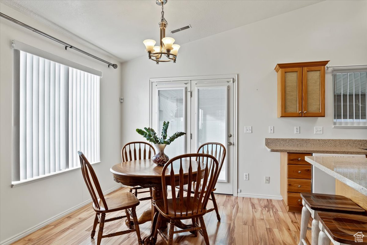 Dining room featuring a wealth of natural light, light hardwood / wood-style floors, vaulted ceiling, and an inviting chandelier