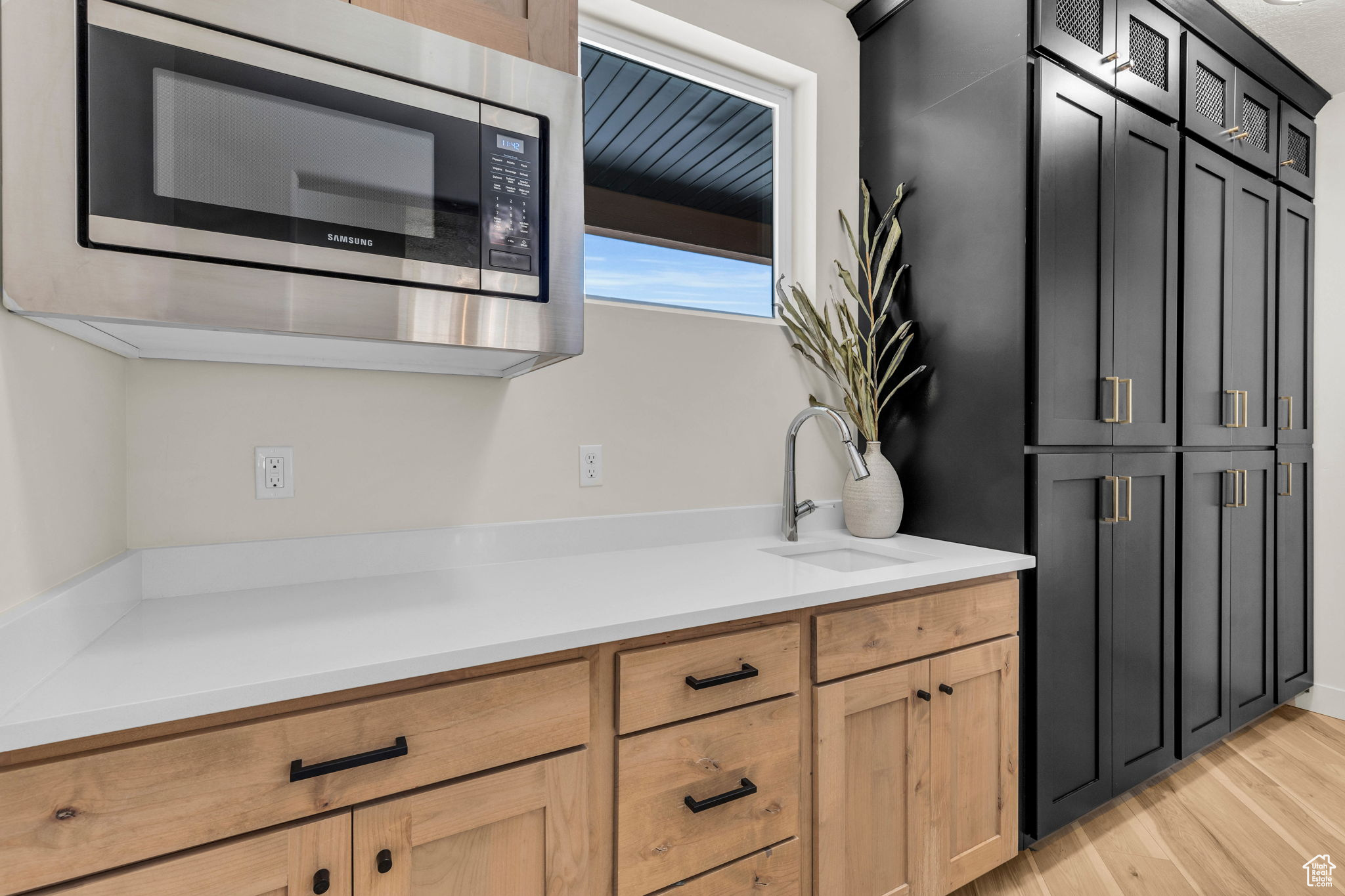 Kitchen featuring light brown cabinetry, stainless steel microwave, light hardwood / wood-style flooring, and sink