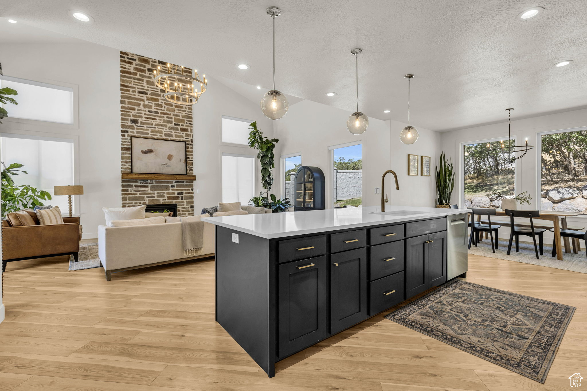 Kitchen featuring sink, a center island with sink, light hardwood / wood-style flooring, dishwasher, and hanging light fixtures