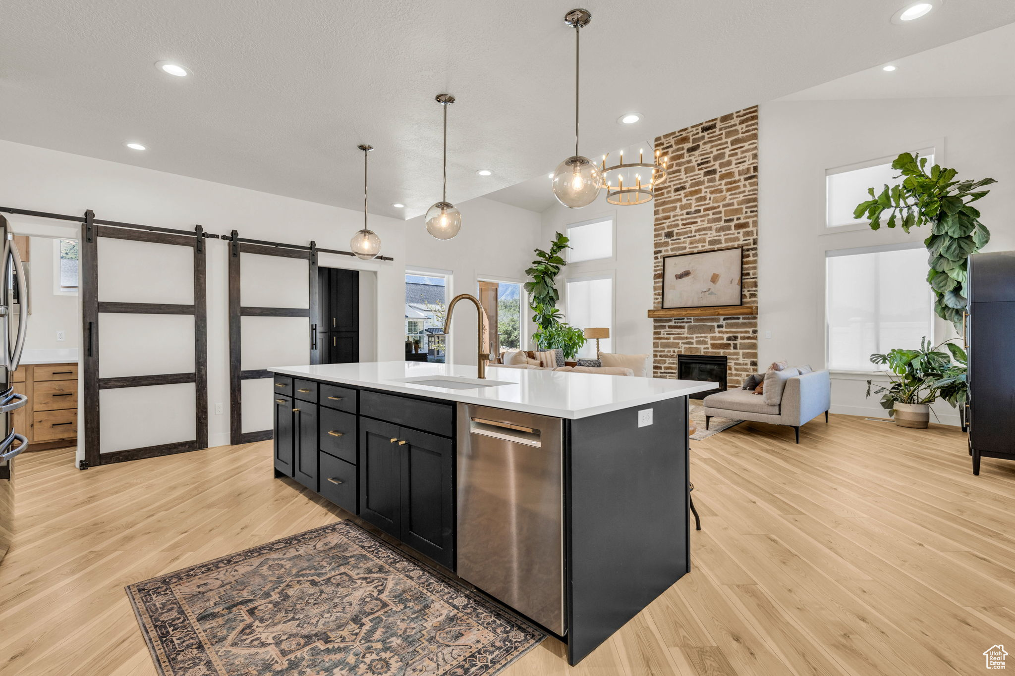 Kitchen featuring sink, stainless steel dishwasher, a barn door, an island with sink, and decorative light fixtures