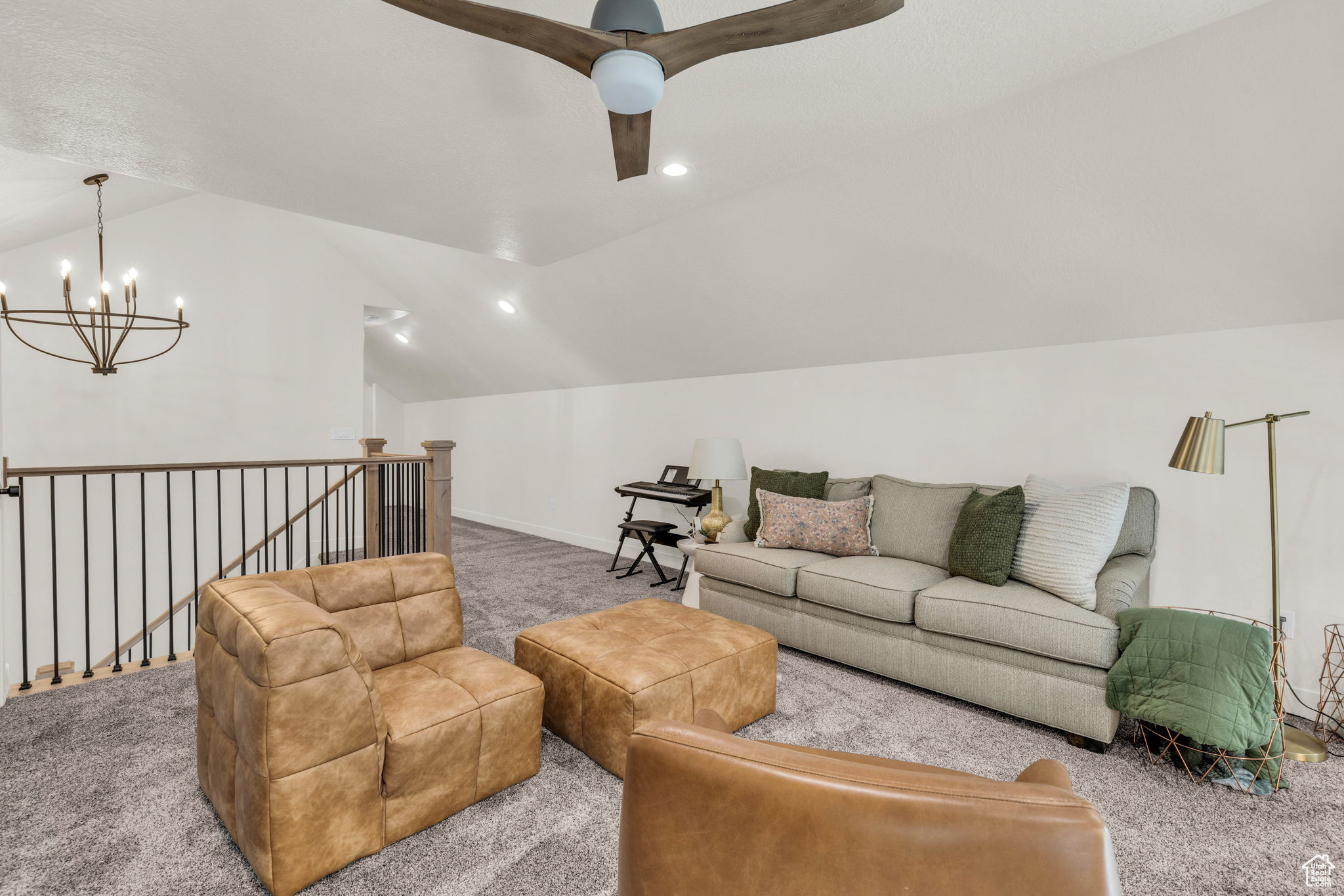 Carpeted living room with lofted ceiling and ceiling fan with notable chandelier