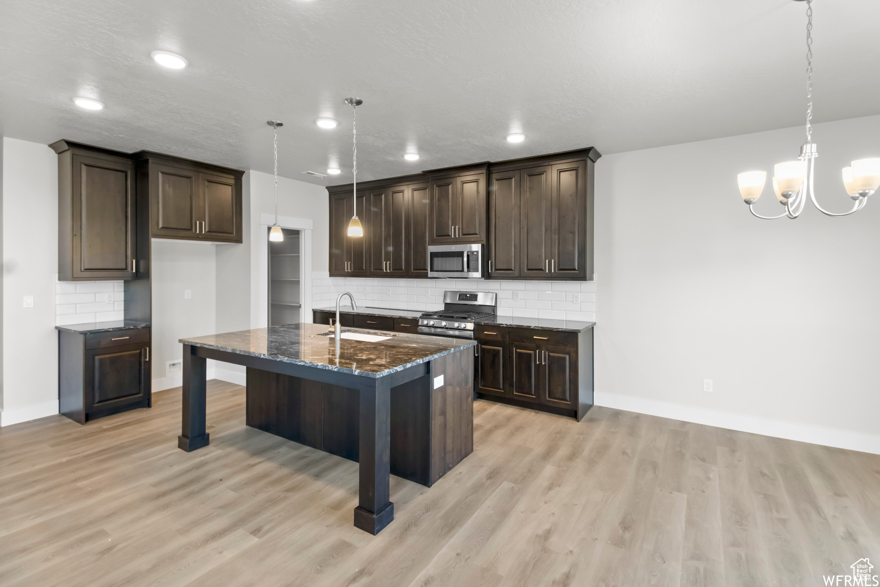 Kitchen with stainless steel appliances, sink, decorative light fixtures, dark stone countertops, and an island with sink