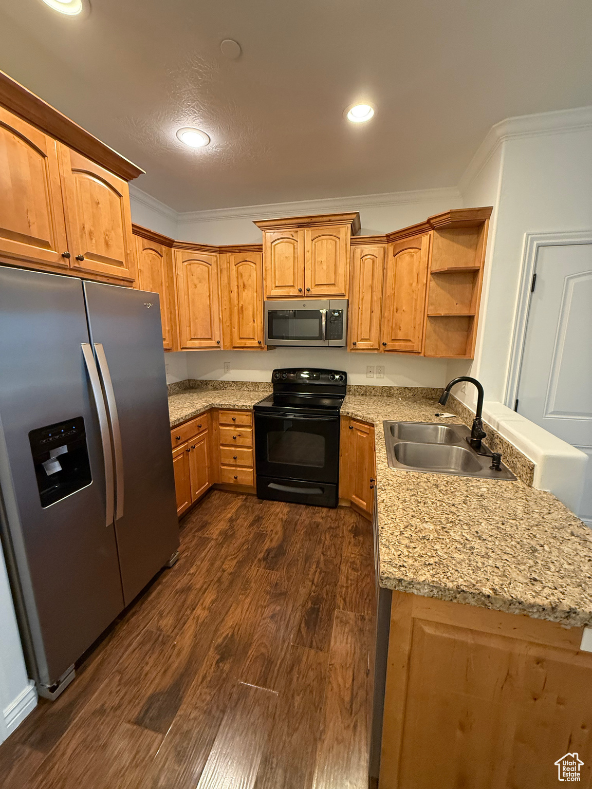 Kitchen with light stone countertops, sink, stainless steel appliances, dark hardwood / wood-style flooring, and ornamental molding