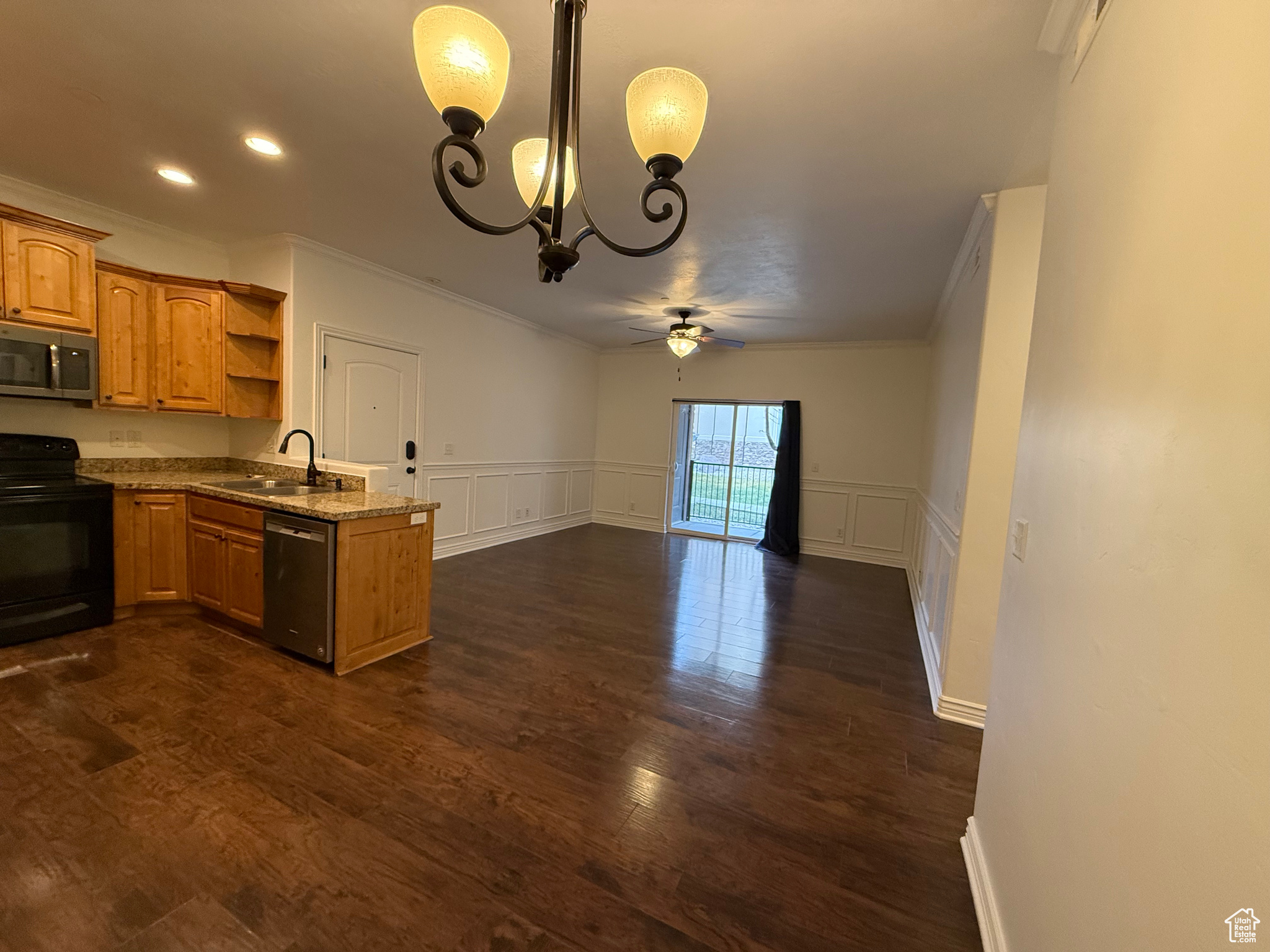 Kitchen with appliances with stainless steel finishes, light stone counters, ceiling fan with notable chandelier, sink, and pendant lighting