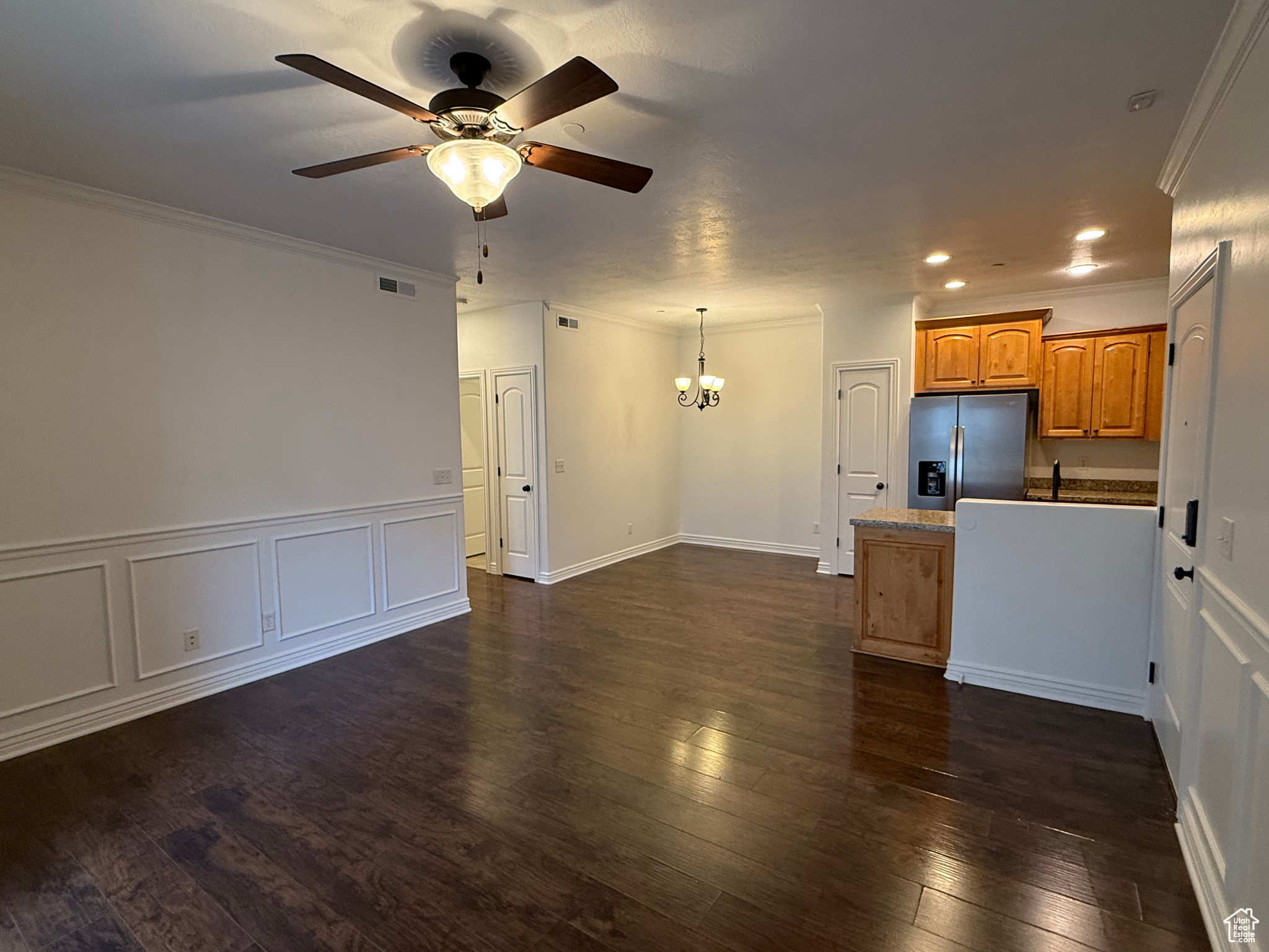 Kitchen featuring dark hardwood / wood-style flooring, ornamental molding, ceiling fan with notable chandelier, pendant lighting, and stainless steel fridge with ice dispenser