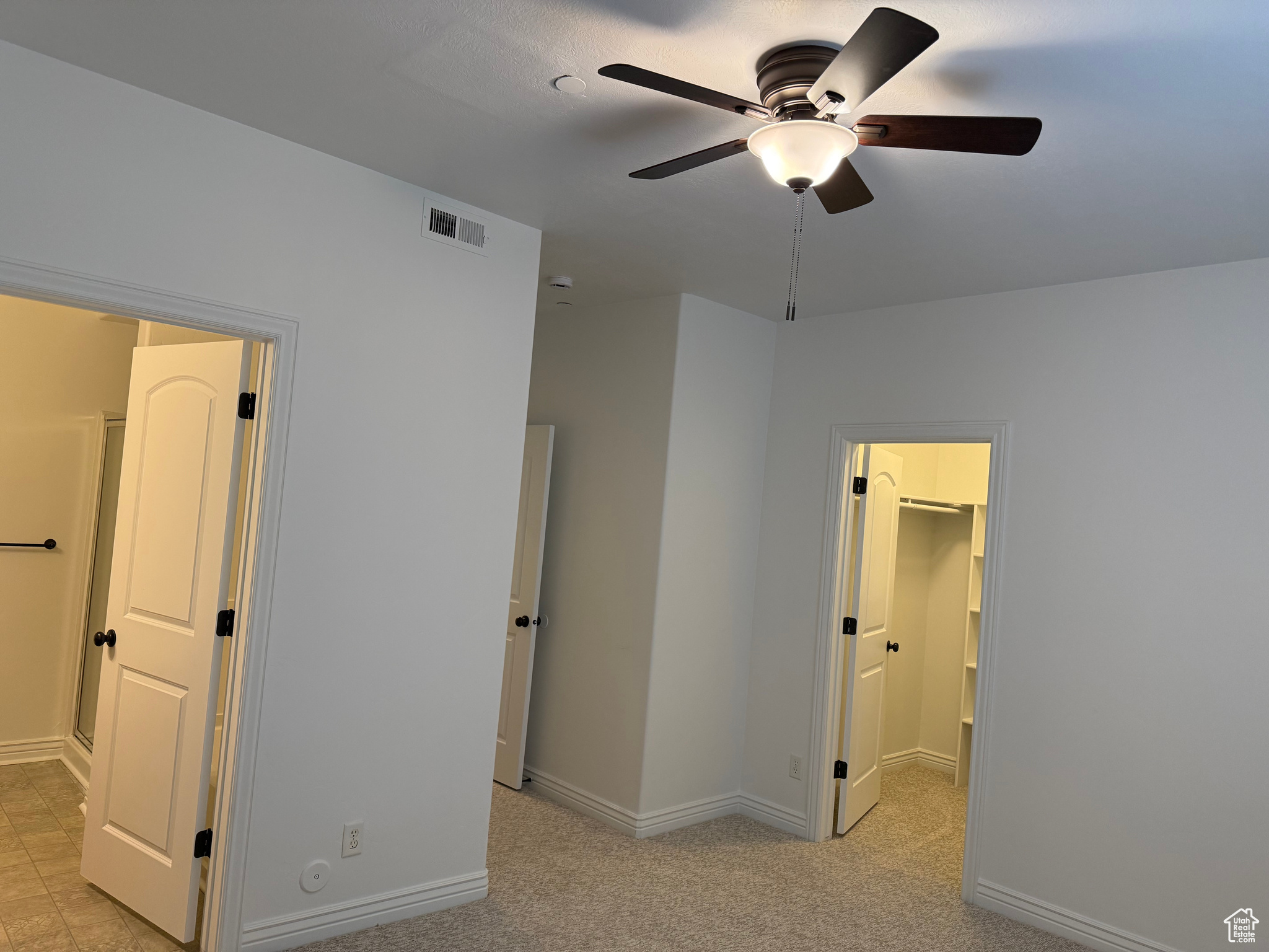 Unfurnished bedroom featuring a closet, a walk in closet, light colored carpet, and ceiling fan