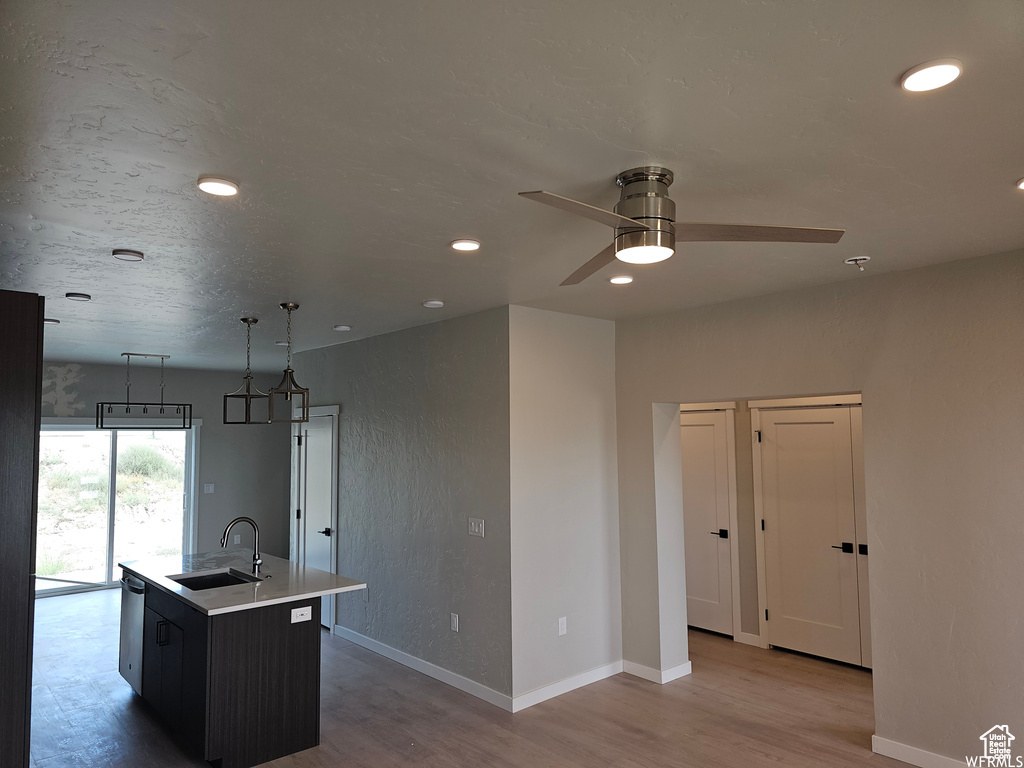 Kitchen featuring stainless steel dishwasher, ceiling fan, a kitchen island with sink, sink, and light hardwood / wood-style floors