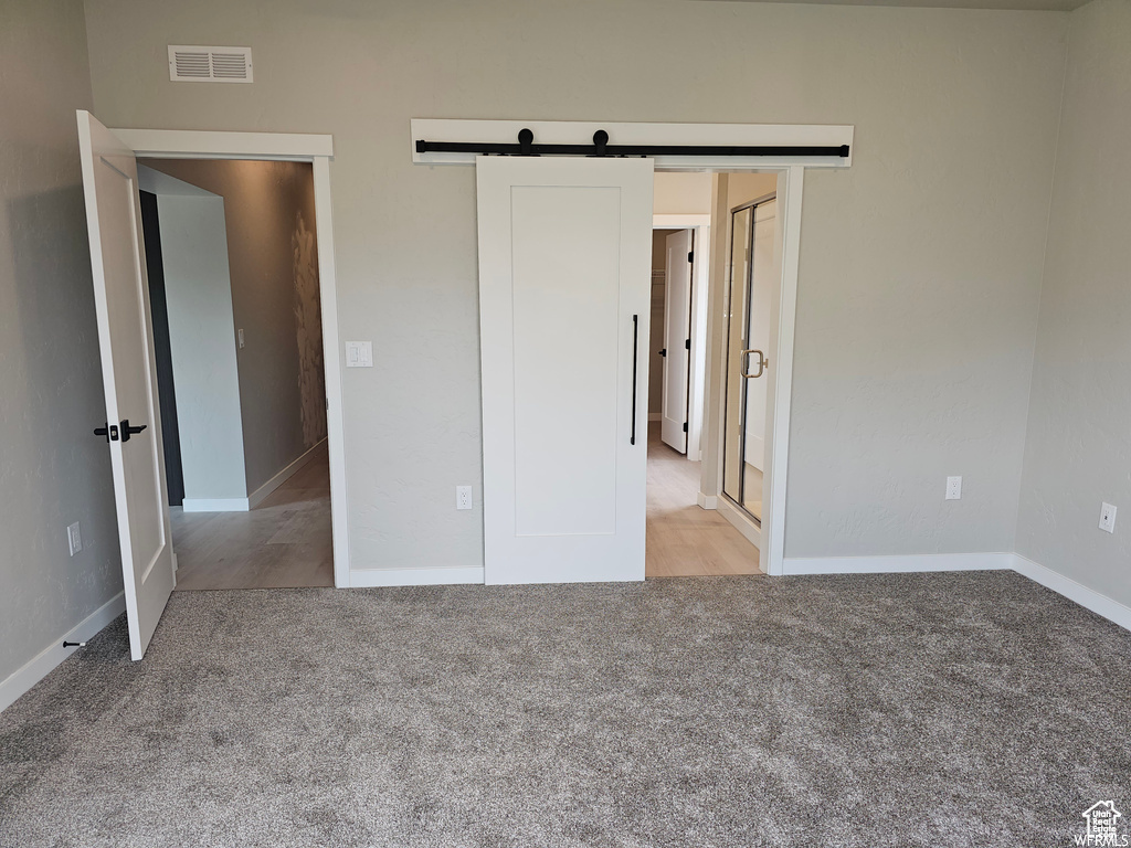 Unfurnished bedroom with light carpet and a barn door