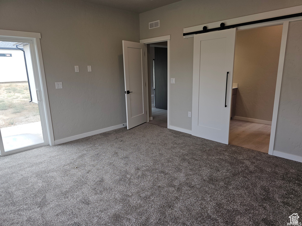 Unfurnished bedroom featuring carpet, a barn door, and access to exterior