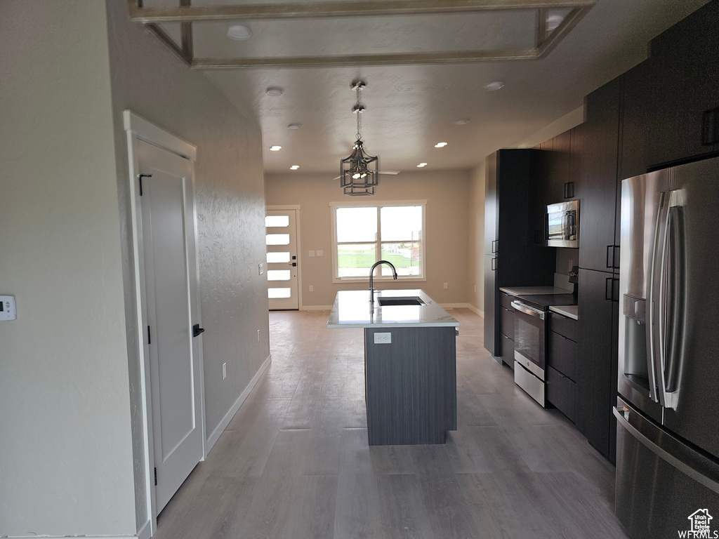 Kitchen featuring appliances with stainless steel finishes, a kitchen island with sink, sink, light hardwood / wood-style flooring, and a notable chandelier