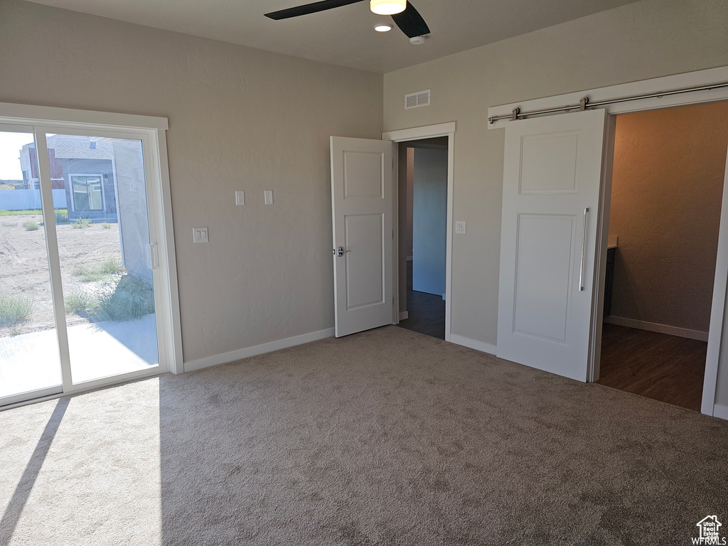 Unfurnished bedroom featuring ceiling fan, a barn door, access to exterior, and carpet floors