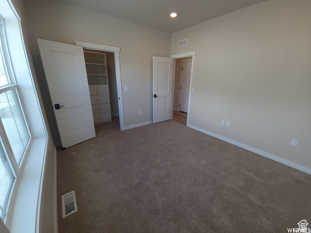 Unfurnished bedroom featuring a walk in closet, carpet floors, and a closet