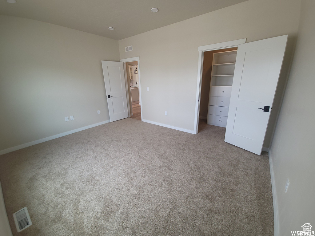 Unfurnished bedroom featuring light colored carpet, a spacious closet, and a closet