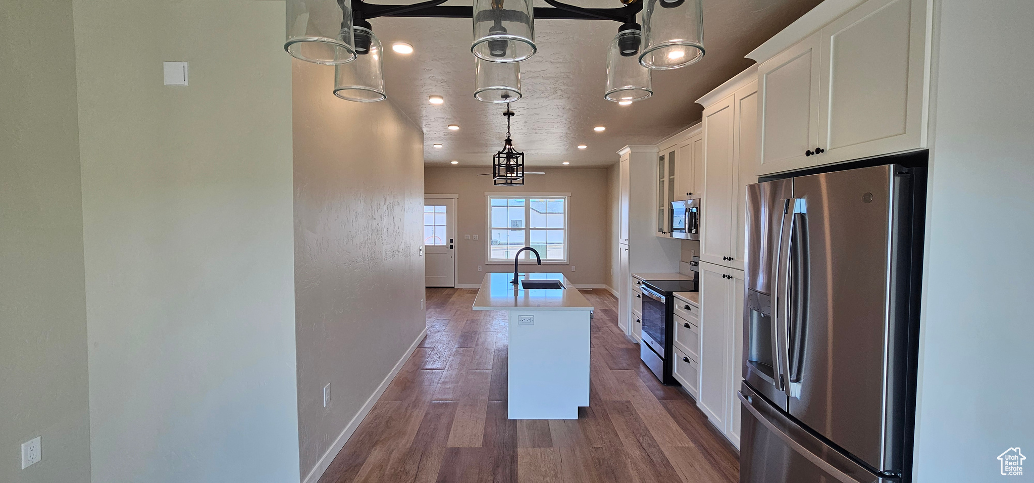 Kitchen with white cabinetry, sink, dark hardwood / wood-style flooring, an island with sink, and appliances with stainless steel finishes