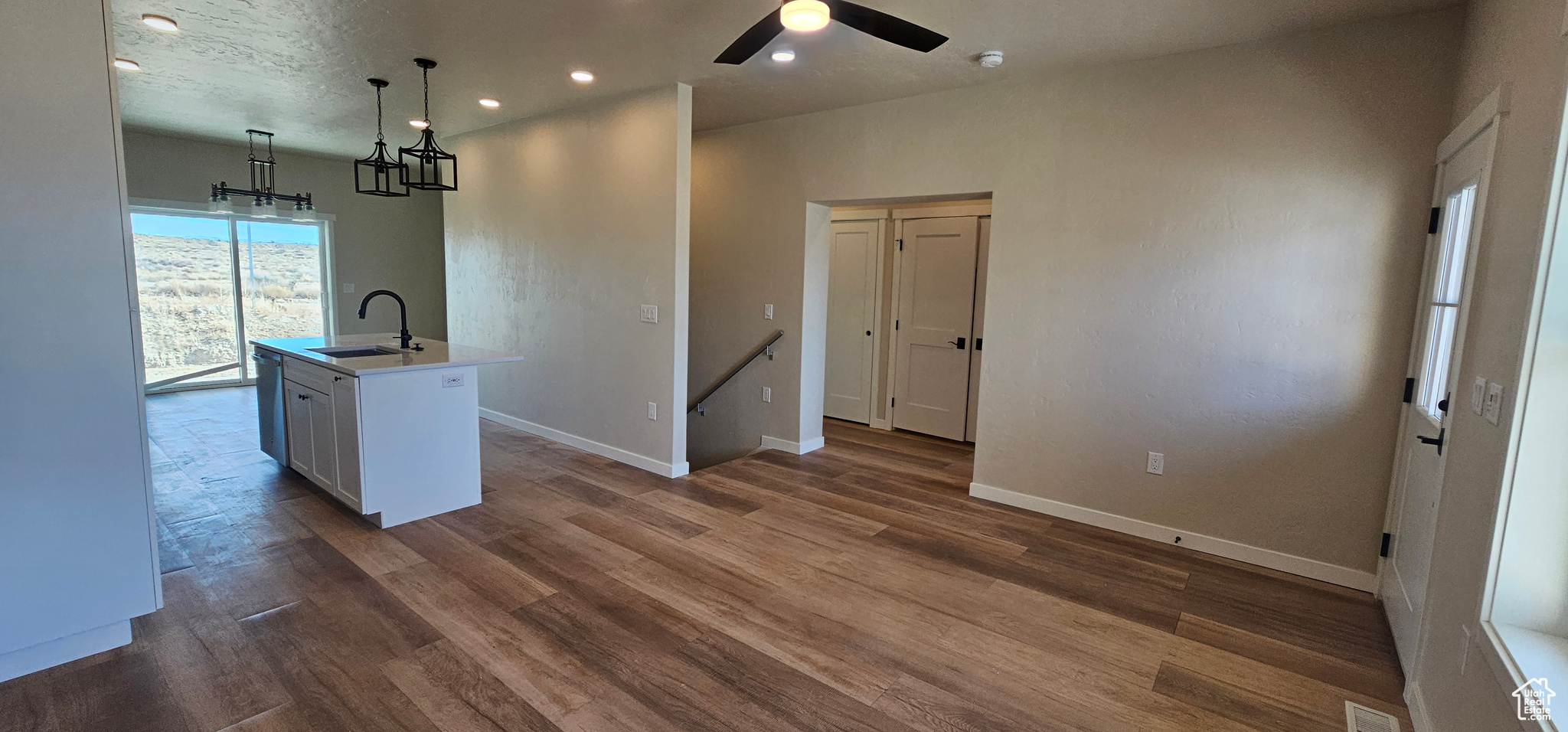 Kitchen featuring dark wood-type flooring, a center island with sink, sink, ceiling fan, and decorative light fixtures