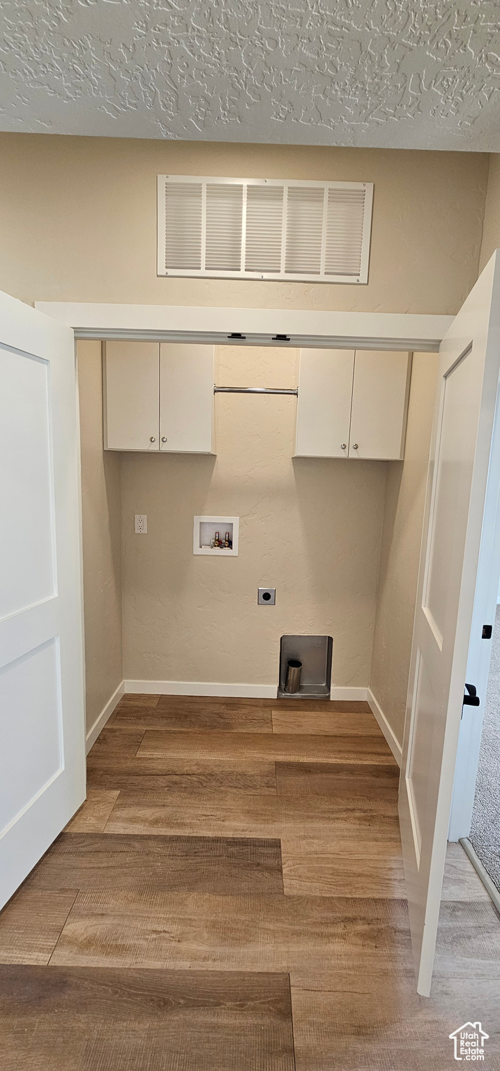 Laundry area with electric dryer hookup, cabinets, washer hookup, light wood-type flooring, and a textured ceiling