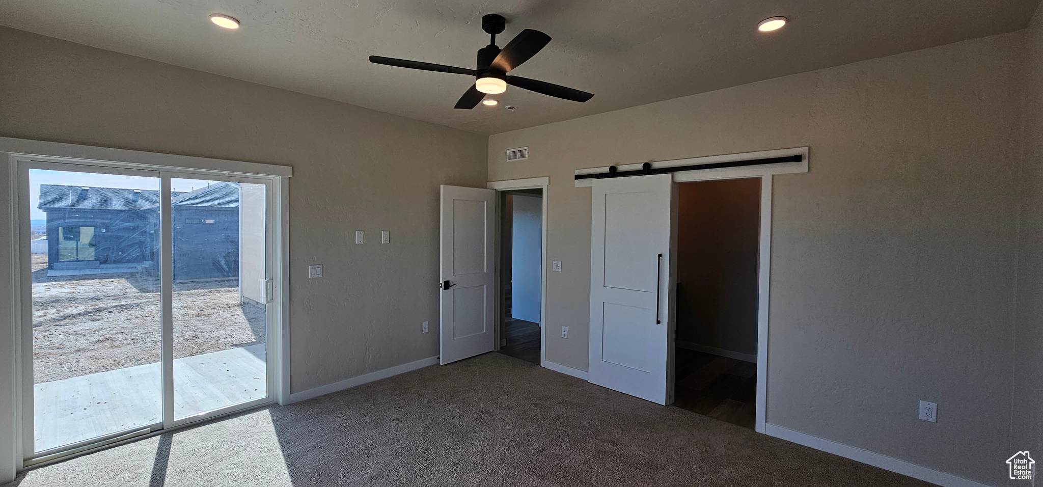 Unfurnished bedroom featuring ceiling fan, a barn door, access to exterior, and carpet floors