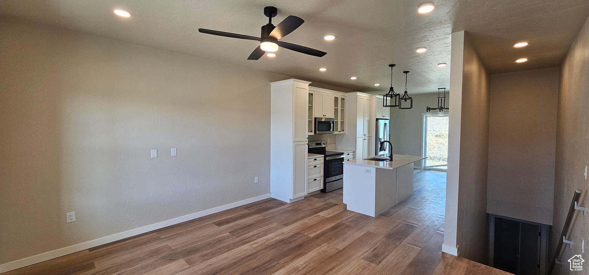 Kitchen with ceiling fan, decorative light fixtures, a kitchen island with sink, white cabinets, and appliances with stainless steel finishes