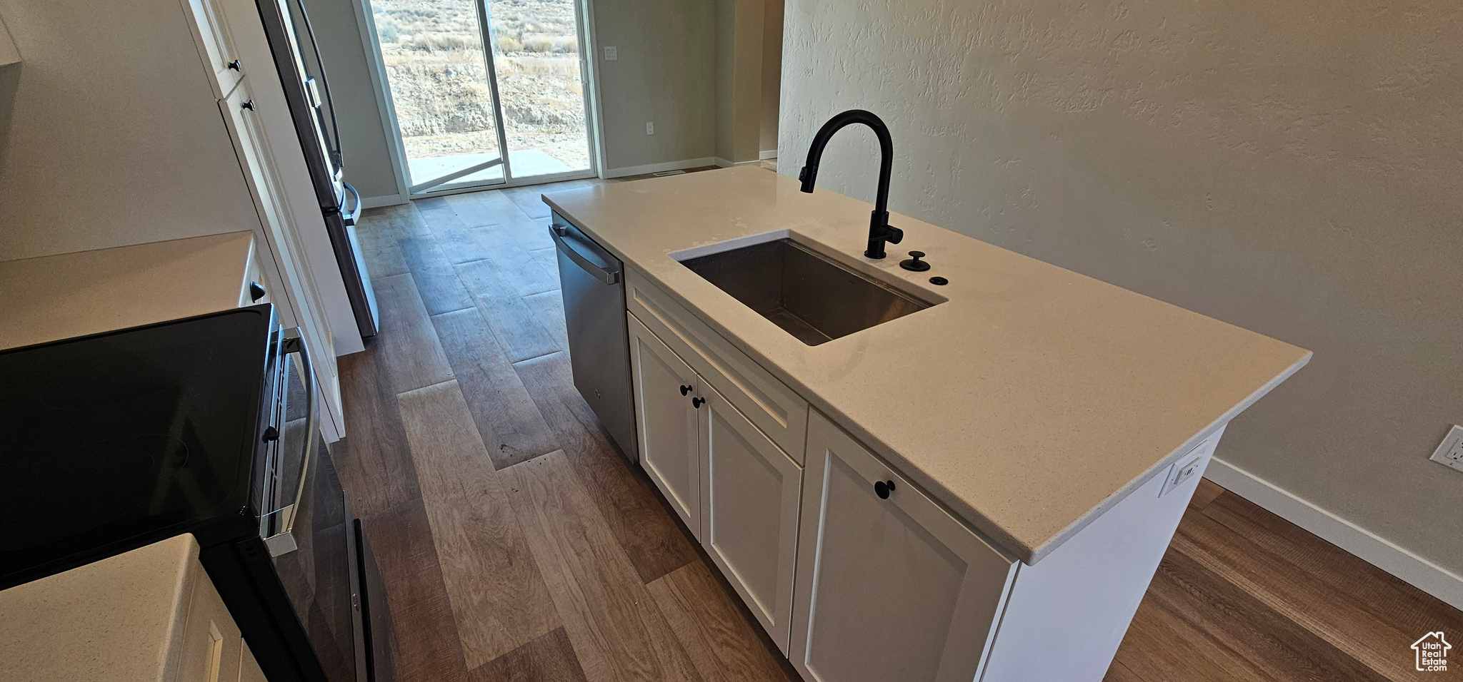 Kitchen featuring a kitchen island with sink, sink, stainless steel dishwasher, white cabinetry, and wood-type flooring