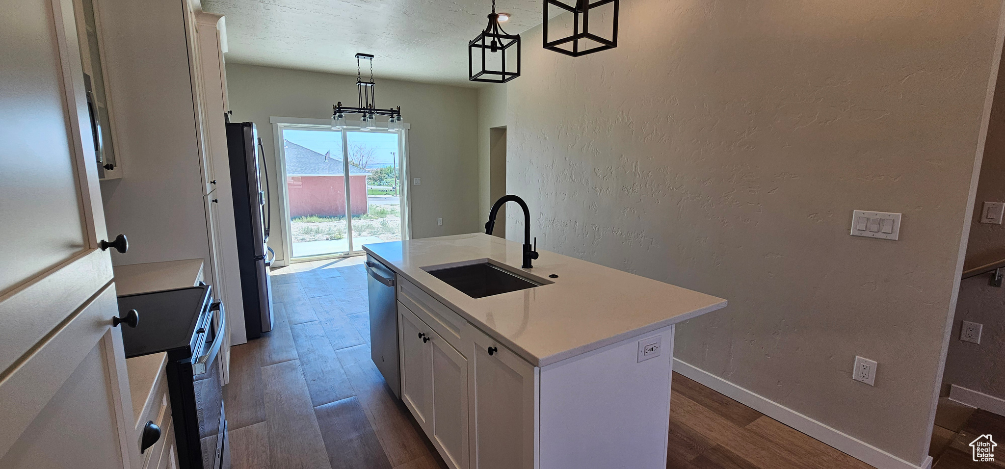 Kitchen featuring stainless steel appliances, a kitchen island with sink, sink, white cabinetry, and hanging light fixtures