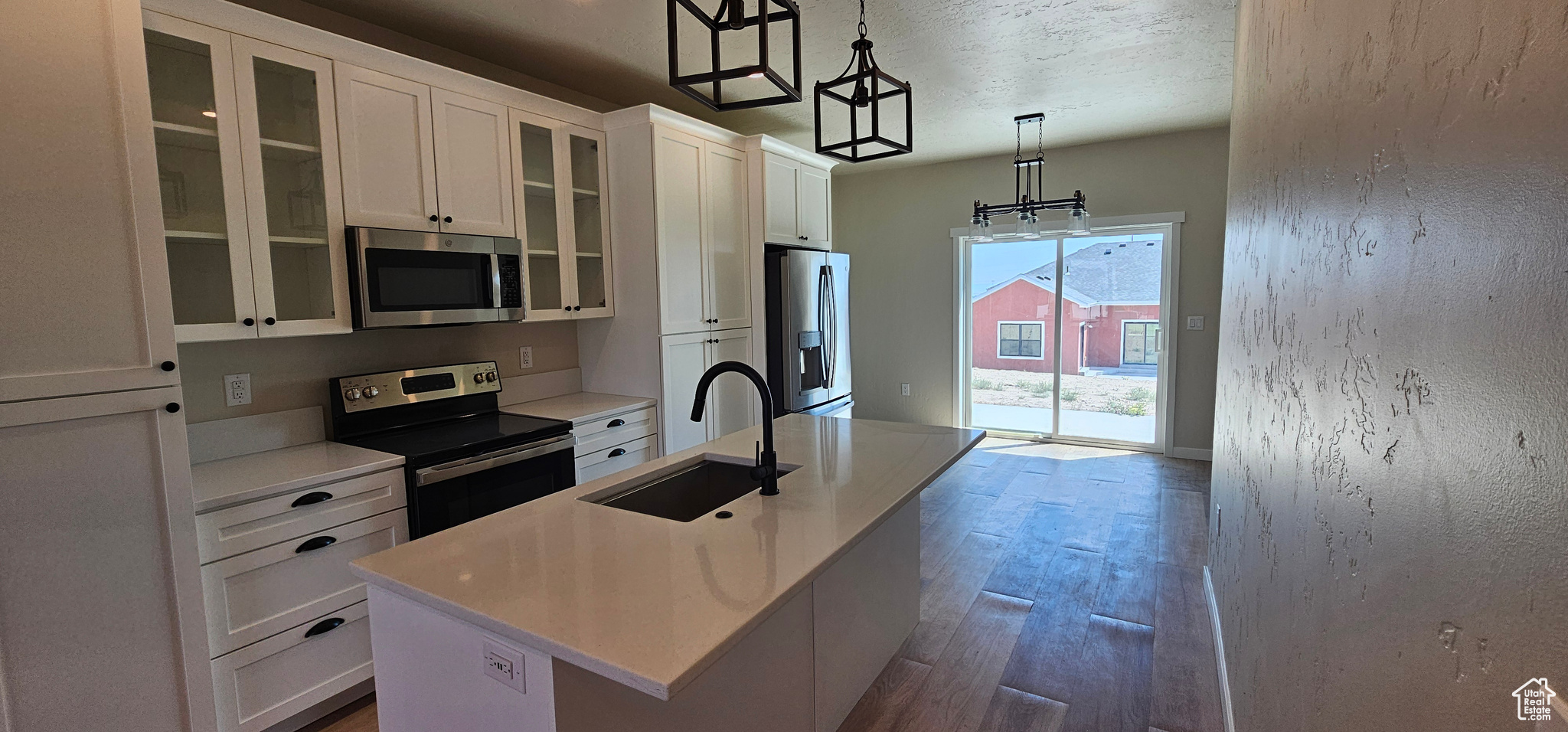 Kitchen featuring a kitchen island with sink, white cabinets, hanging light fixtures, sink, and stainless steel appliances