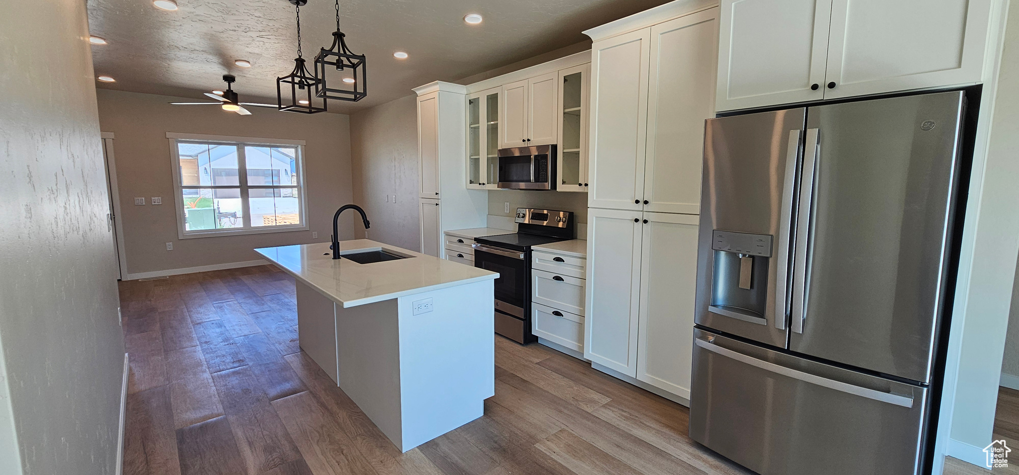 Kitchen with white cabinetry, sink, stainless steel appliances, an island with sink, and decorative light fixtures