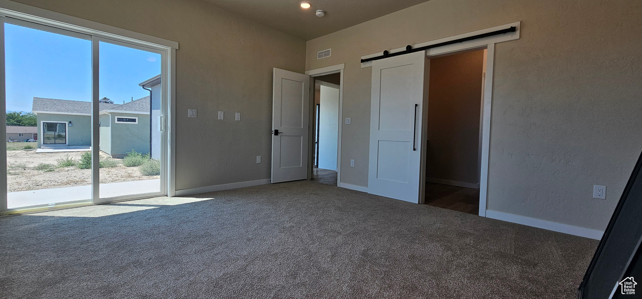 Unfurnished bedroom with carpet flooring, a barn door, and access to exterior