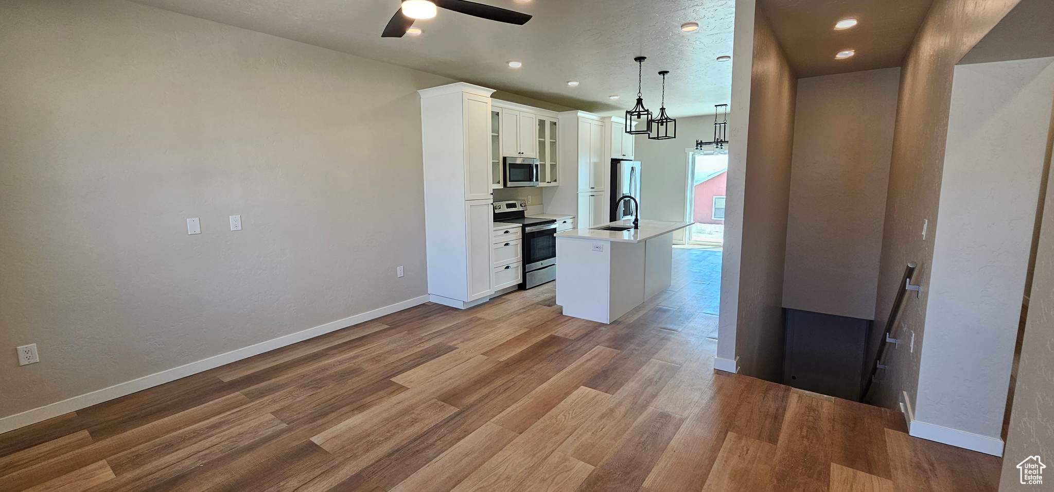 Kitchen featuring white cabinetry, a kitchen island with sink, hanging light fixtures, and appliances with stainless steel finishes