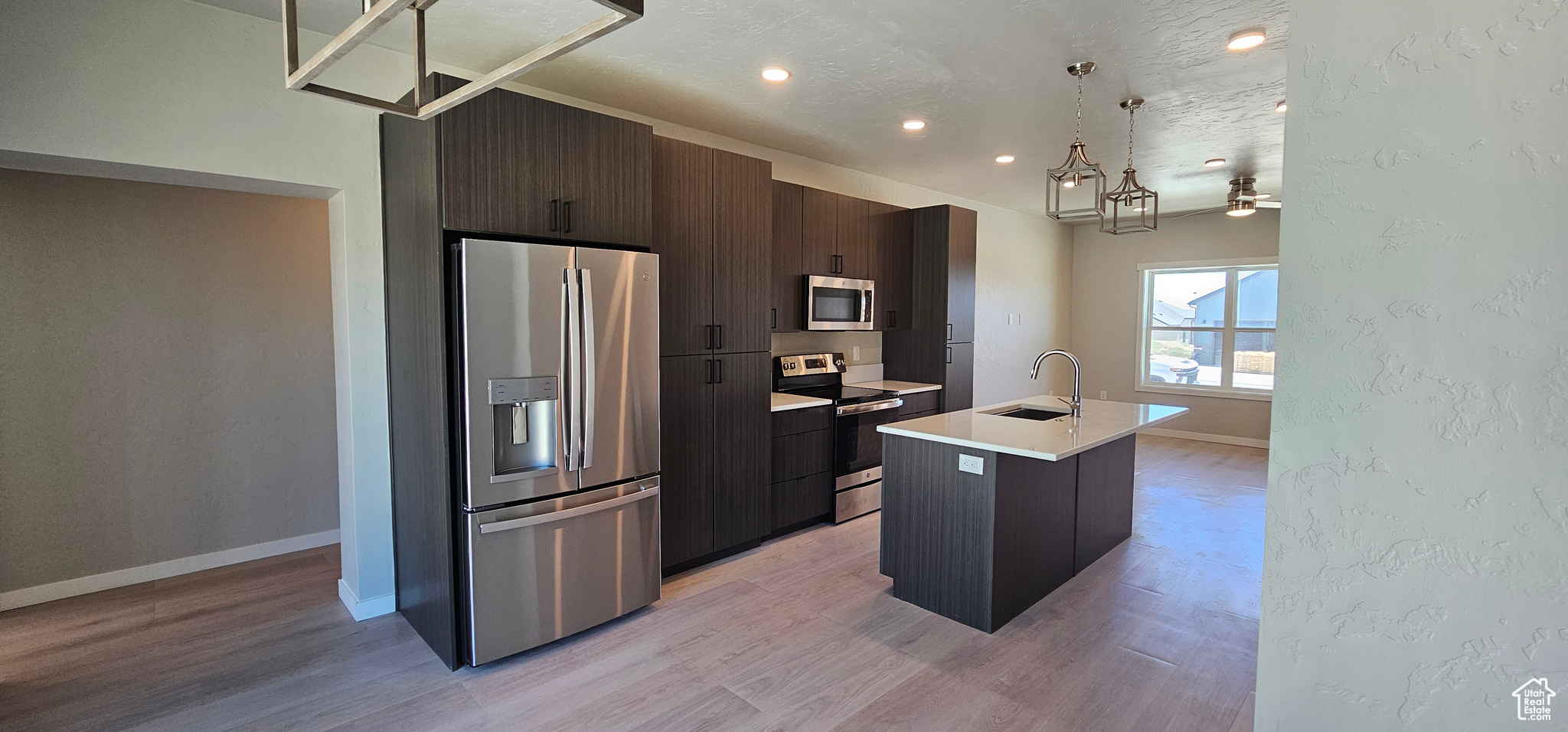 Kitchen featuring light hardwood / wood-style floors, stainless steel appliances, hanging light fixtures, and an island with sink