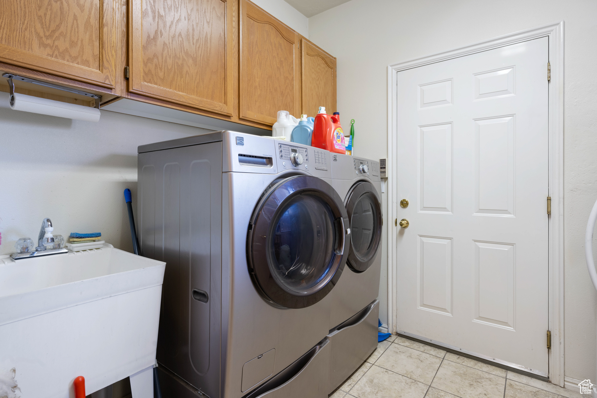 Laundry room with washer and dryer, light tile patterned flooring, cabinets, and sink