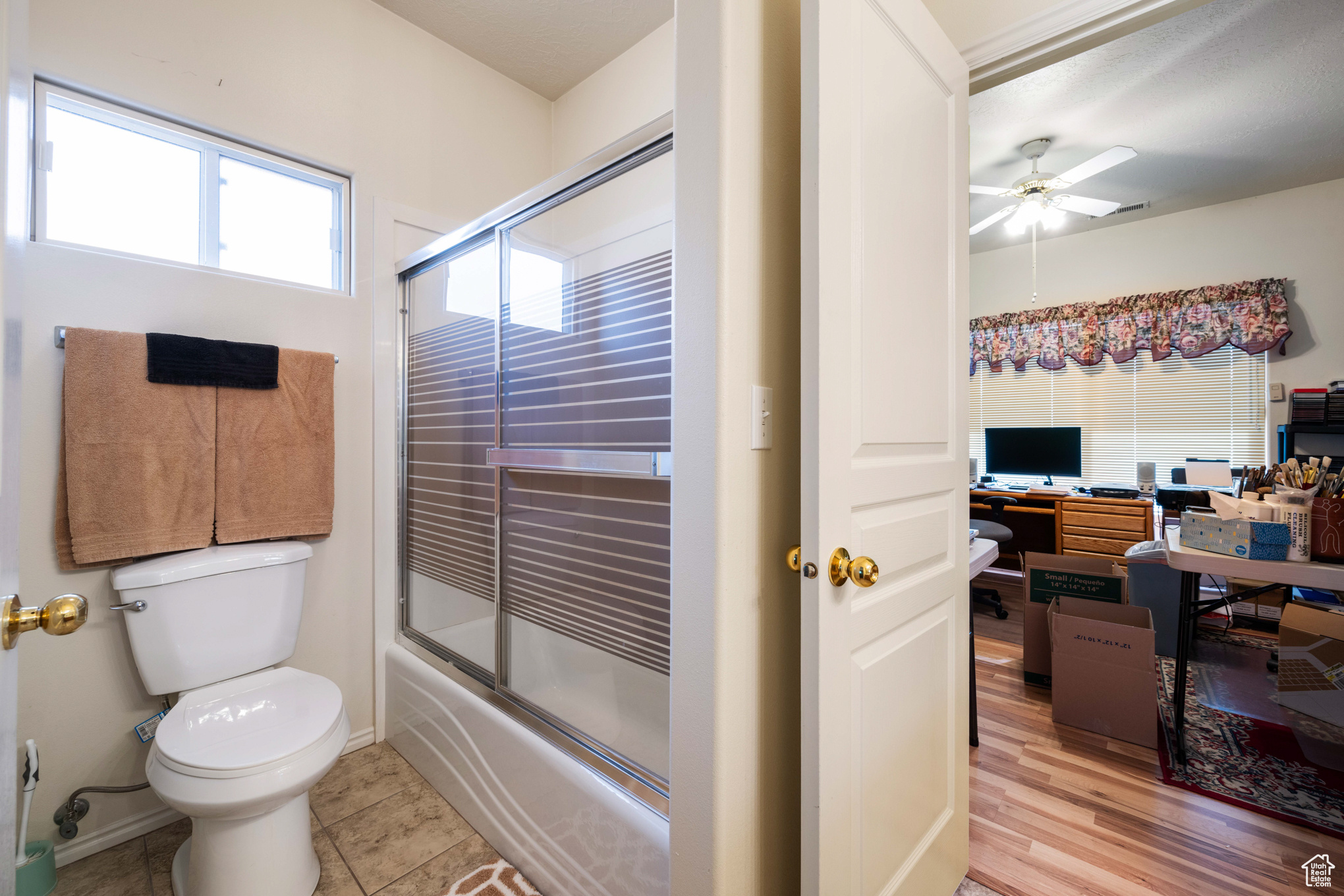 Bathroom featuring tile patterned flooring, toilet, ceiling fan, and bath / shower combo with glass door