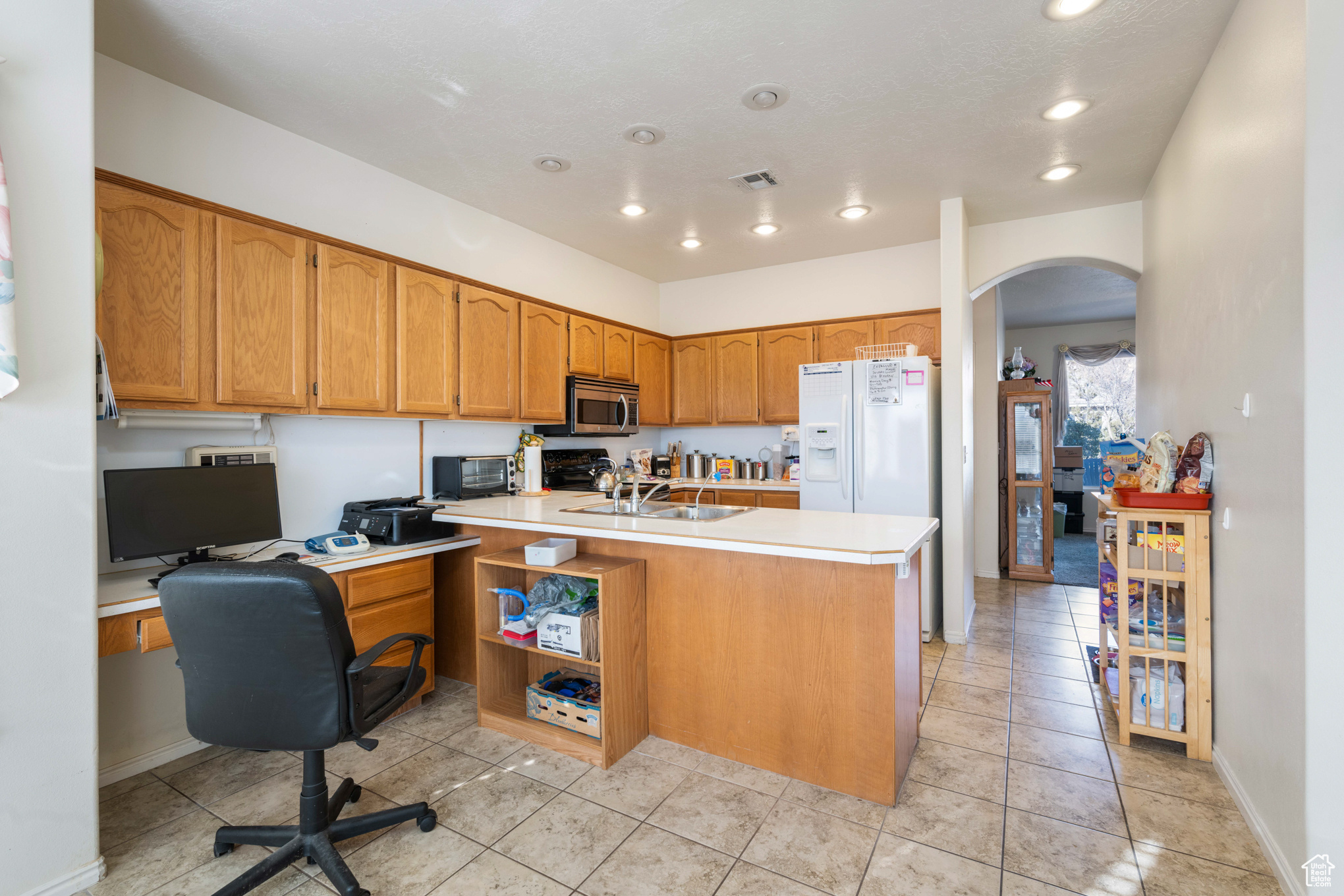 Kitchen with a center island with sink, light tile patterned floors, sink, and white refrigerator with ice dispenser